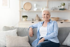 Relaxed Elderly Woman Posing On Couch Im Cozy Home Interior.